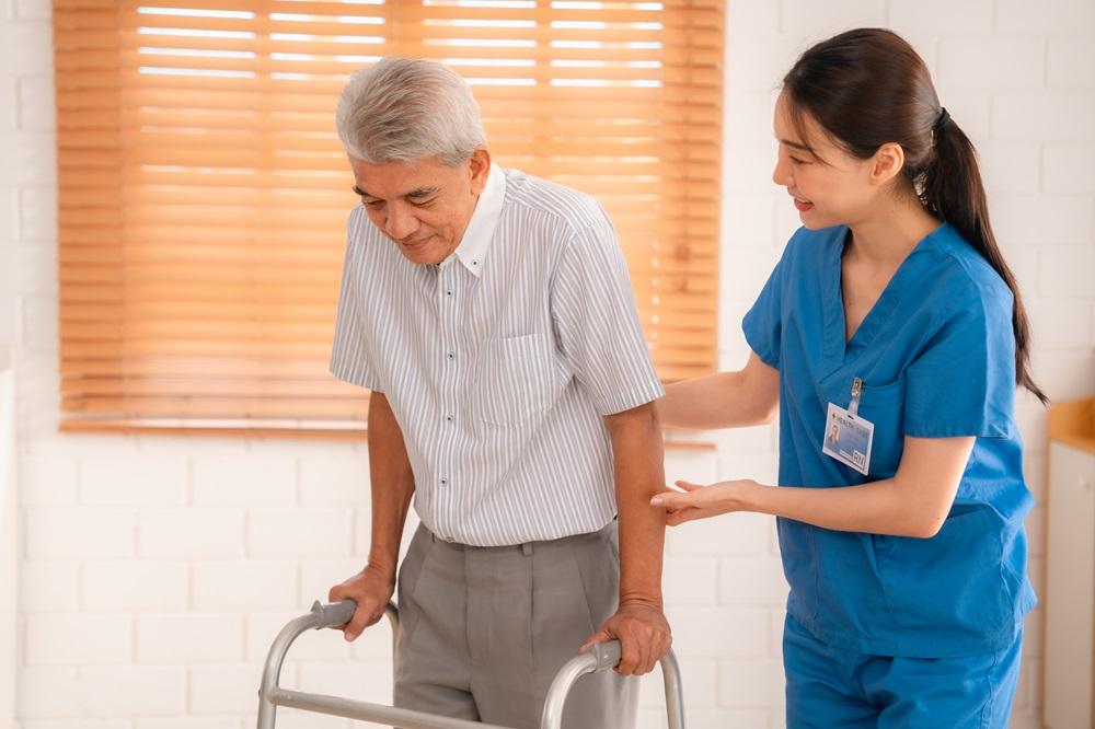 Home caregiver helping an elderly patient walk using a walker